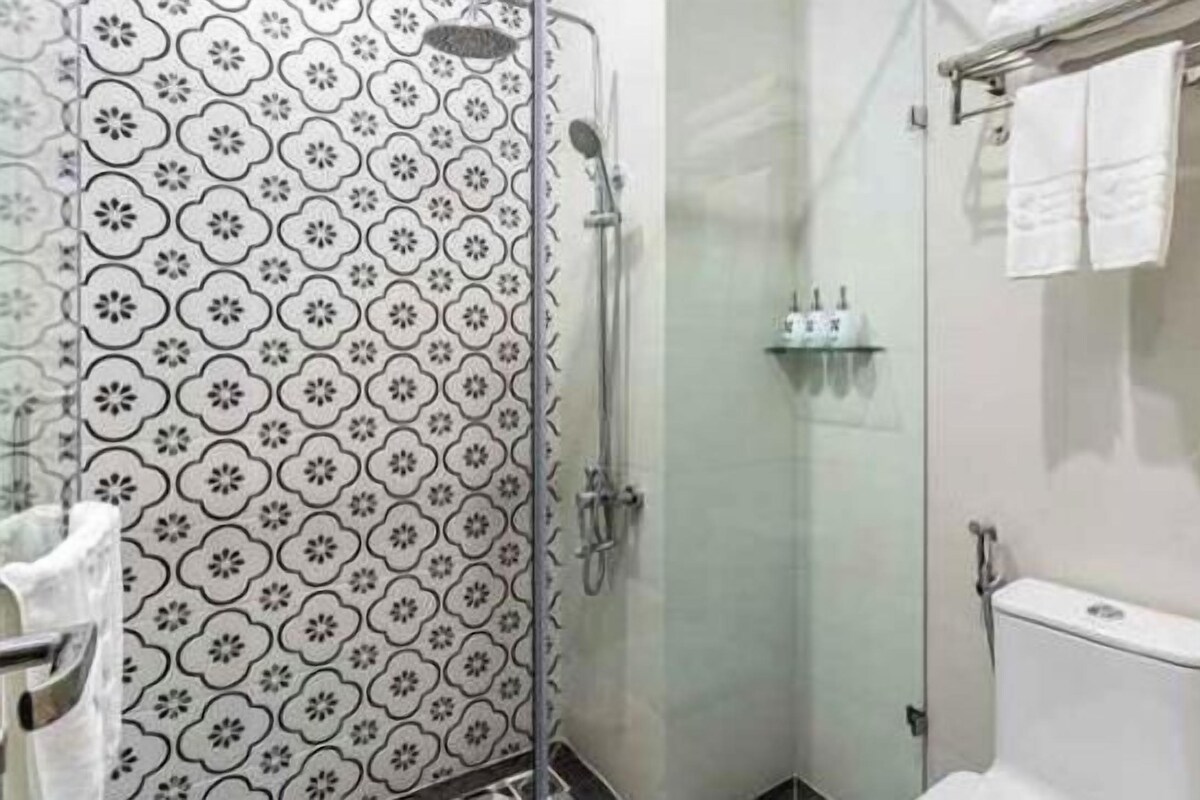 A bathroom with a patterned wall, a glass shower enclosure, a toilet, and a towel rack.