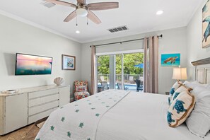 Un dormitorio con cama, ventilador de techo, televisor, escritorio y vistas al exterior.