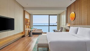 Ein Hotelzimmer mit einem großen Bett, einem Fernseher, einer Sitzecke mit Meerblick und einer Wand mit Holzelementen.