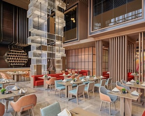 A modern restaurant with tiered seating, a central decorative wall, and a view of the cityscape. - Hyatt Regency Shanghai Lingang (Shanghai)