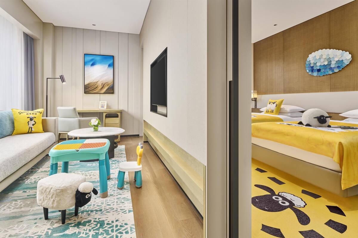 Une chambre d’hôtel moderne, équipée d’un canapé, d’un petit bureau, d’un lit avec une couvre-lit jaune et d’un téléviseur fixé au mur.