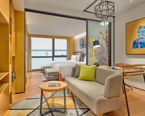 Een moderne hotelkamer met een groot raam, een bank, een eettafel en een klein bijzettafeltje.