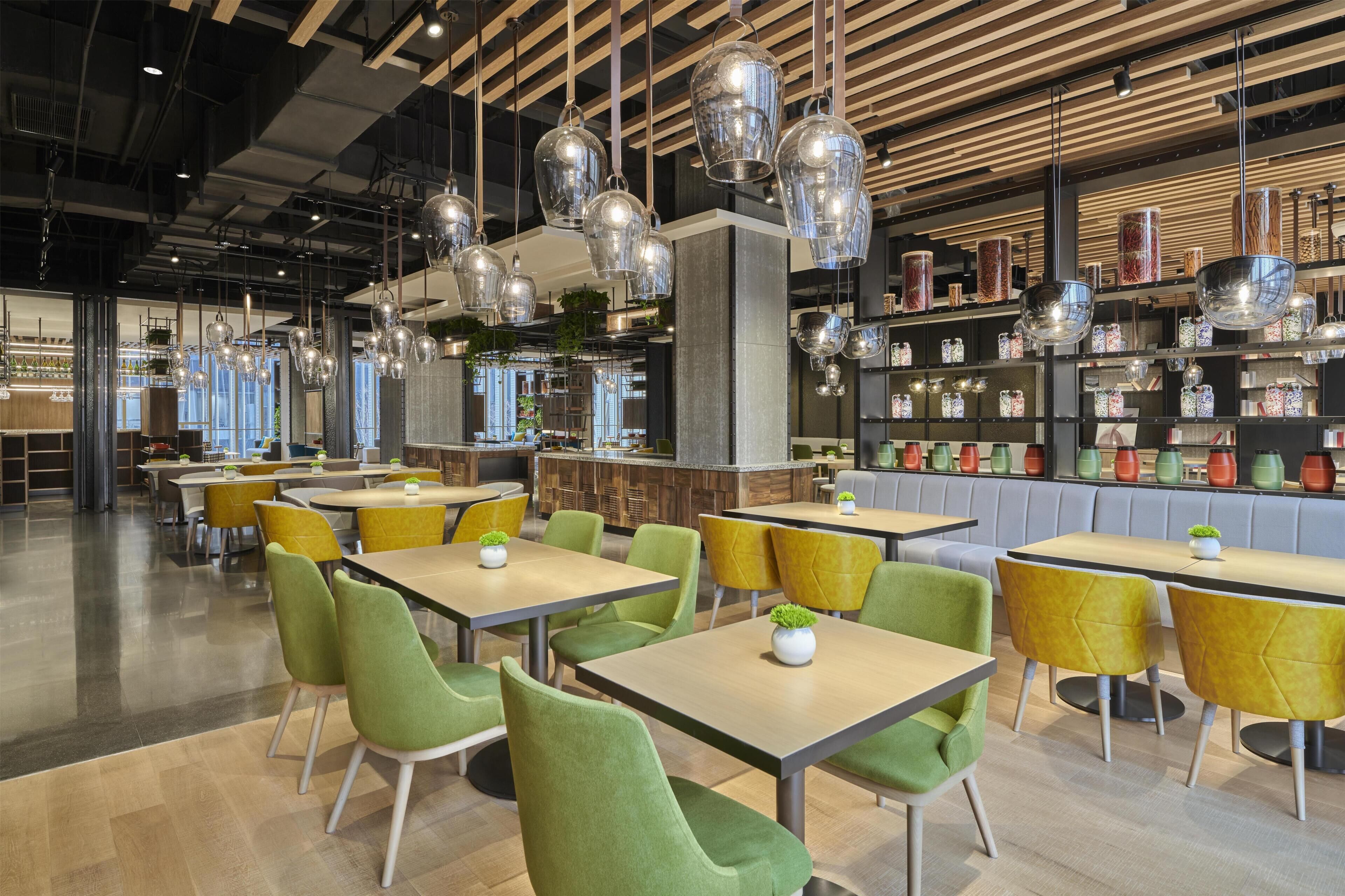 A modern restaurant interior with green and yellow chairs, hanging light fixtures, and a bar area.