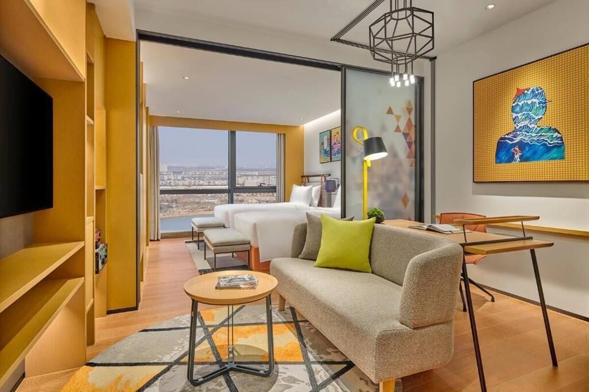 Une chambre d’hôtel moderne équipée d’un canapé, d’une petite table, d’un bureau, d’une télévision et d’une grande fenêtre donnant sur la ville.
