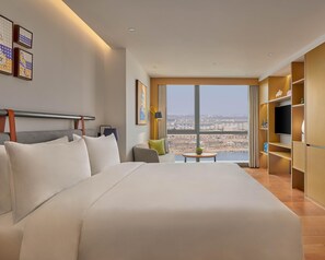 Een hotelkamer met een groot bed, een bureau, een televisie en uitzicht over de stad.