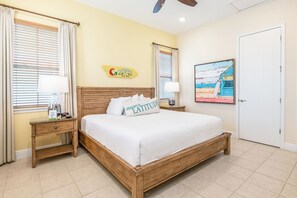 Habitación de hotel con una cama de madera, dos mesitas de noche con lámparas, un reloj de pared, un cuadro enmarcado y una ventana con cortinas.