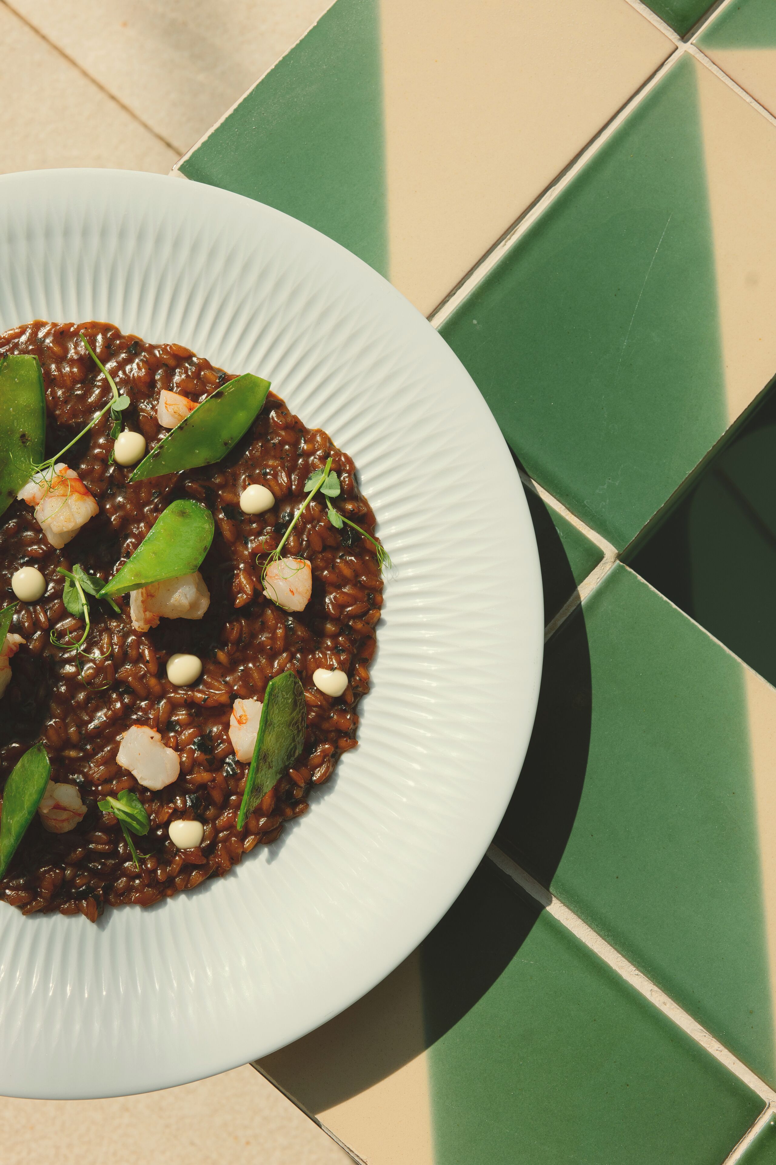 A plate of black risotto garnished with peas and herbs on a white plate.