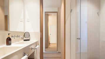Un baño moderno con un espejo grande, un lavamanos con dispensador de jabón, un perchero para toallas y una zona de ducha.