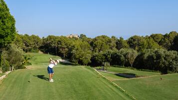 A golf course with a player in mid-swing, surrounded by lush greenery and a clear sky.