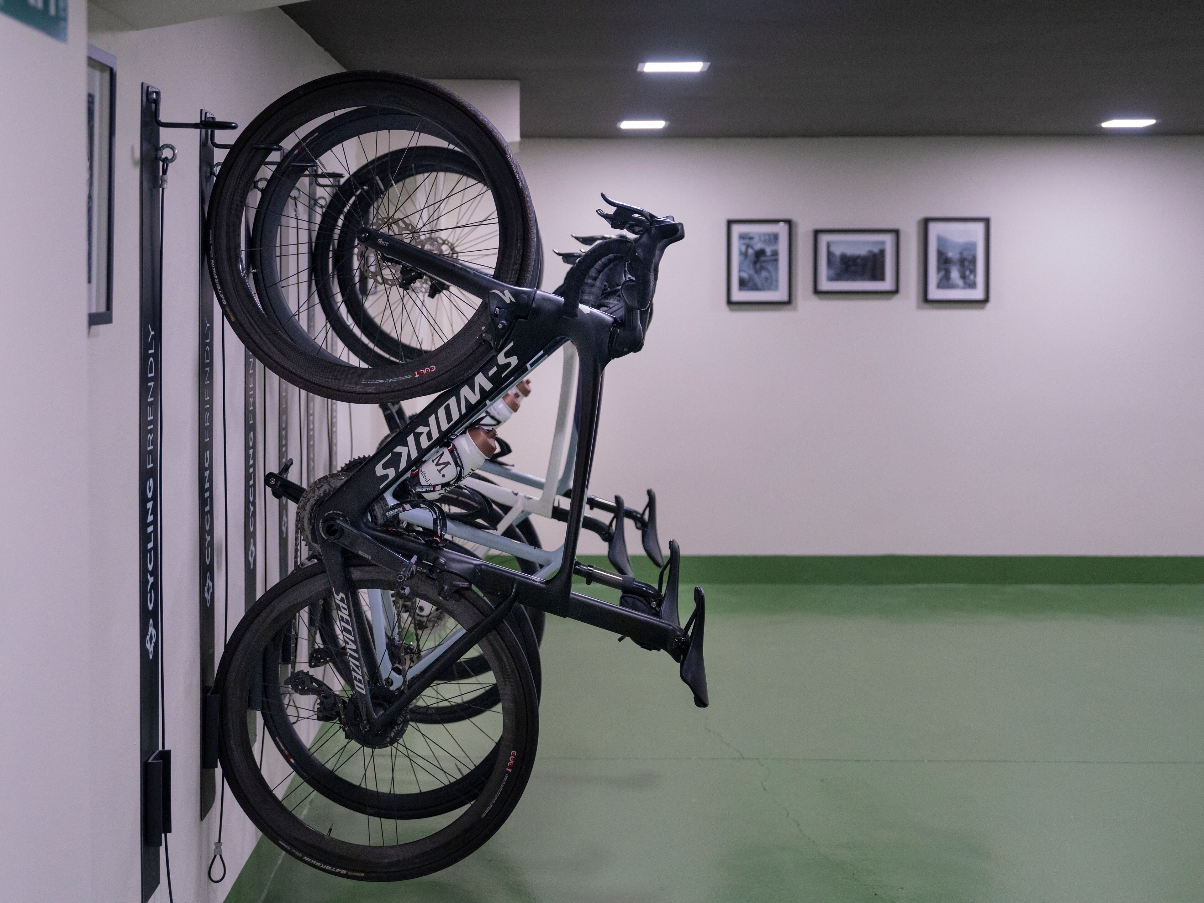 Una bicicletta montata su un supporto a parete in una stanza con pavimento verde e quadri appesi al muro.