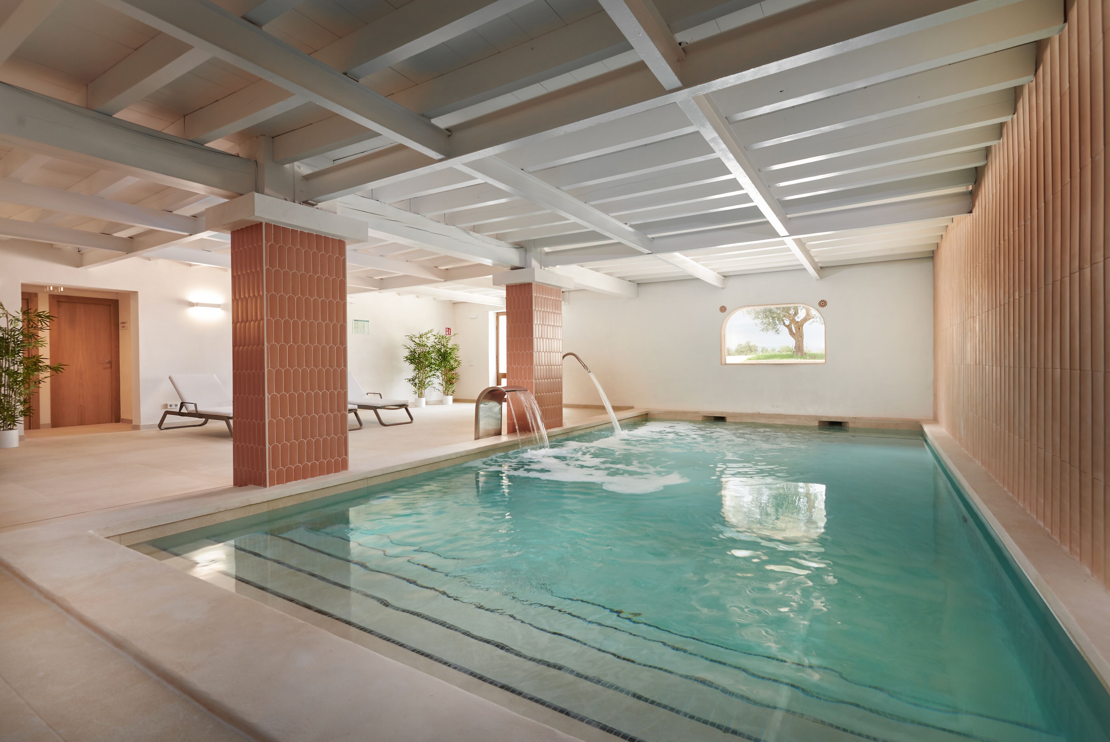 Piscina interna com água cristalina, um pilar de madeira e um banco.