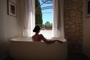 Una persona en una bañera con vista a una pared de piedra y una ventana con cortinas.