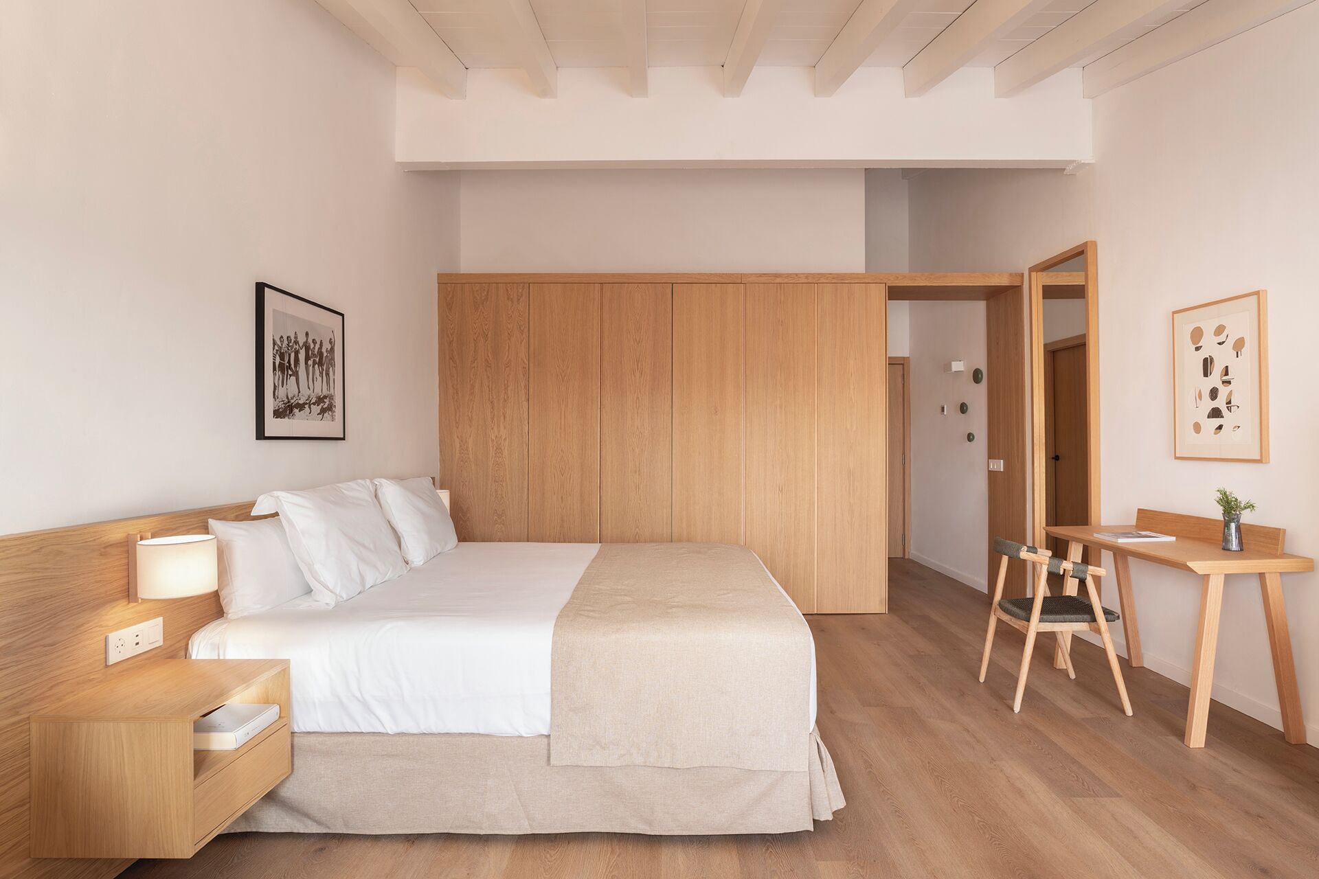 Ein Schlafzimmer mit Bett, Nachttisch, Lampe, Kleiderschrank, Schreibtisch, Stuhl und Kunstwerk.