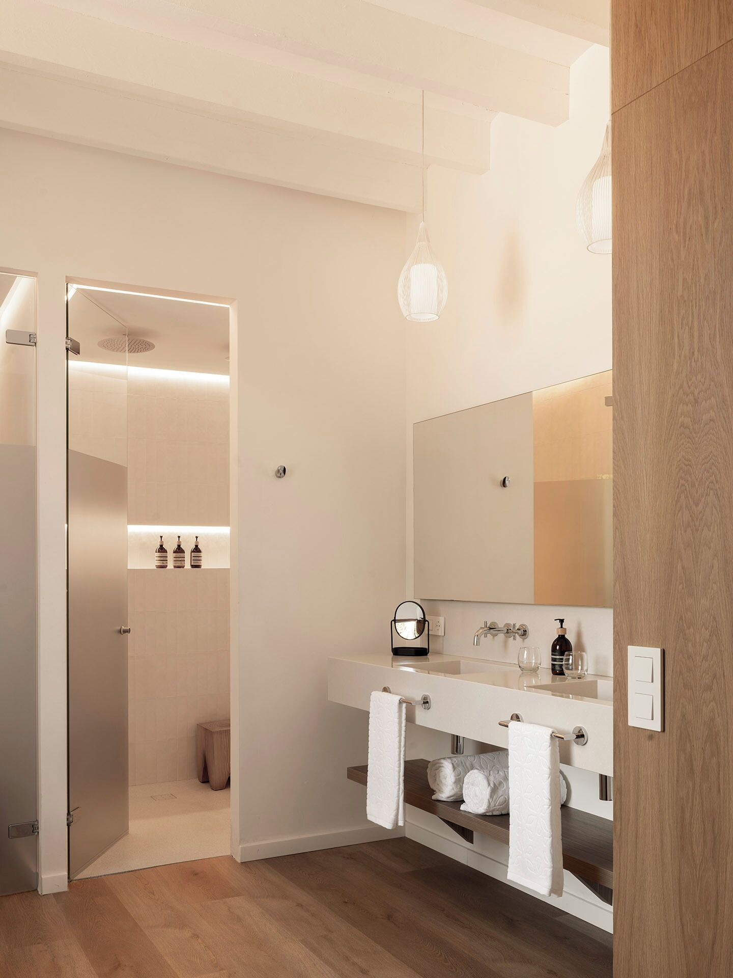 Une salle de bain moderne avec un plancher en bois, un meuble-lavabo blanc avec un miroir et une cabine de douche en verre.