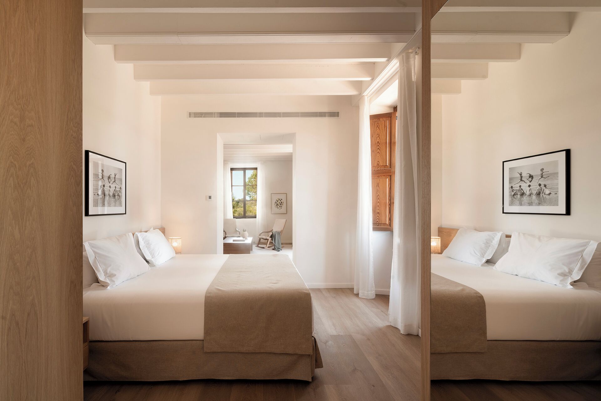 A hotel room with two beds, a wooden floor, and a view of the outdoors through a window.