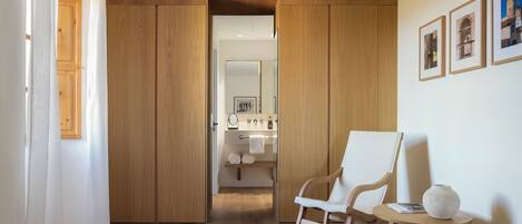 Un baño moderno con muebles de madera, un lavabo blanco y un espejo. Hay un sillón mecedora y una mesita con un florero.