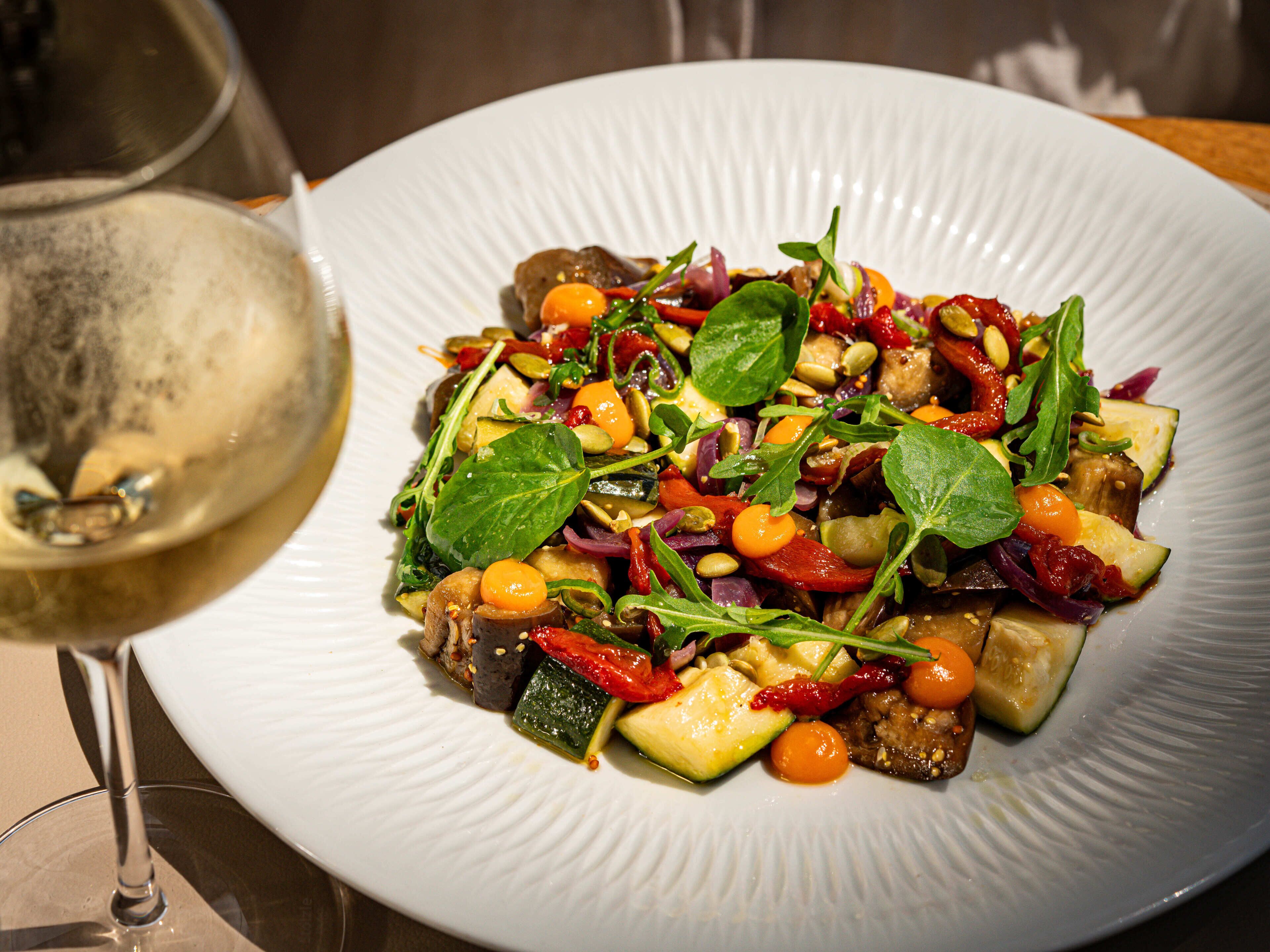 A plate of mixed vegetables and a glass of white wine.