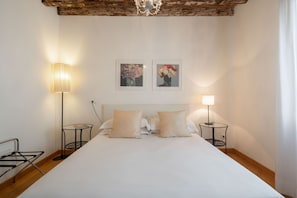A bedroom with a large bed, two bedside lamps, a small table, and two framed pictures on the wall.