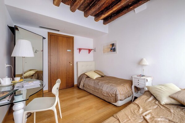 A bedroom with a wooden ceiling, a glass desk, a bed with a headboard, a bedside table, and a chair.