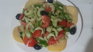 En tallrik spaghetti med köttfärssås och svarta oliver, och en tallrik med blandade grönsaker, inklusive tomater, gurka och oliver.