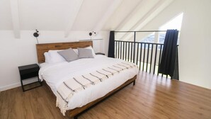 Ein Schlafzimmer mit einem hölzernen Bett, einem Nachttisch, einem schwarzen Geländer und Blick ins Freie.