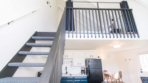 Eine moderne Wohnung mit einer Treppe zu einem Schlafzimmer im oberen Bereich, einer Küche mit blauen Schränken und einem Essbereich mit einer grauen Couch.