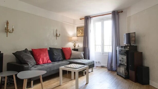 A living room with a grey sofa, two small tables, a television, and a sound system. - Atypical old house in Montreuil. (Montreuil)