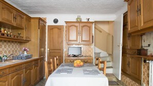 A kitchen with wooden cabinets, a dining table with a fruit bowl, and a television on a stand. - Atypical old house in Montreuil. (Montreuil)