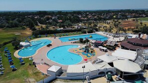 A large swimming pool complex with multiple pools and a water slide, surrounded by lounge chairs and umbrellas.