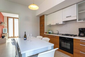 A modern kitchen with white cabinetry, a dining table with chairs, a stove, and a coffee maker.