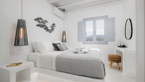 A modern bedroom with a bed, bedside table, wall art, and a window with a view. - Xerolithos Natural Living (Naxos)