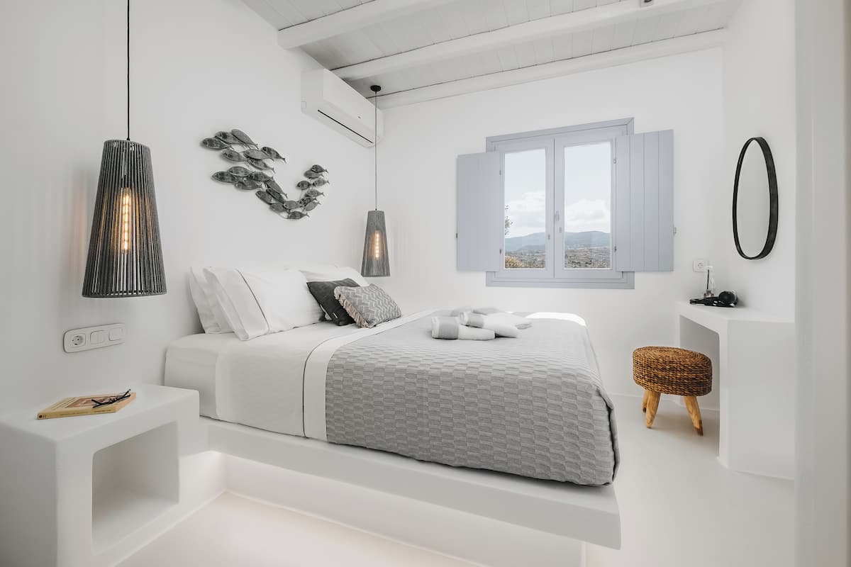 A modern bedroom with a bed, bedside table, wall art, and a window with a view.