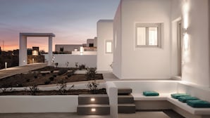 A modern building with white walls, a stone pathway, and a seating area with cushions. - Xerolithos Natural Living (Naxos)