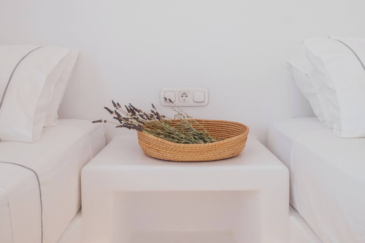 A minimalist room with a white sofa, a small white table with a woven basket, and two abstract wall art pieces.