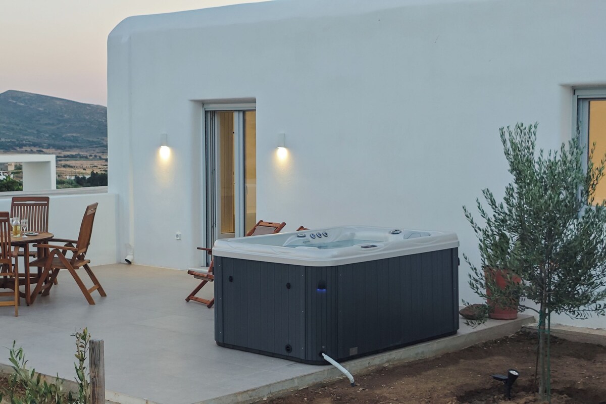Een hottub op een terras met een tafel, stoelen, een deur en uitzicht op het landschap.