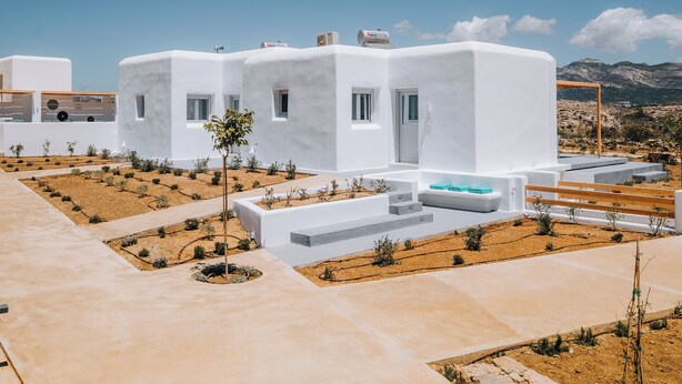 A modern white building with multiple rooms, a swimming pool, and a view of mountains. - Xerolithos Natural Living (Naxos)