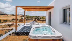 A hot tub under a wooden pergola with a table and chairs, overlooking a vineyard. - Xerolithos Natural Living (Naxos)