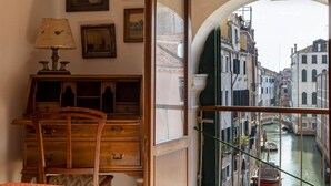 Ein Zimmer mit einem Holztisch, einem Stuhl und einer Lampe. Ein Fenster bietet Blick auf einen Kanal und Gebäude.
