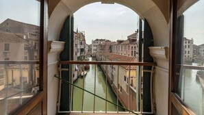 Blick durch ein Rundbogenfenster auf einen Kanal in einer historischen Stadt, mit Gebäuden entlang des Wasserwegs.