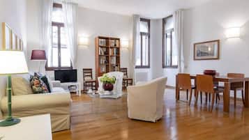 Un soggiorno con divano, tavolino, libreria, tavolo da pranzo con sedie e televisione.