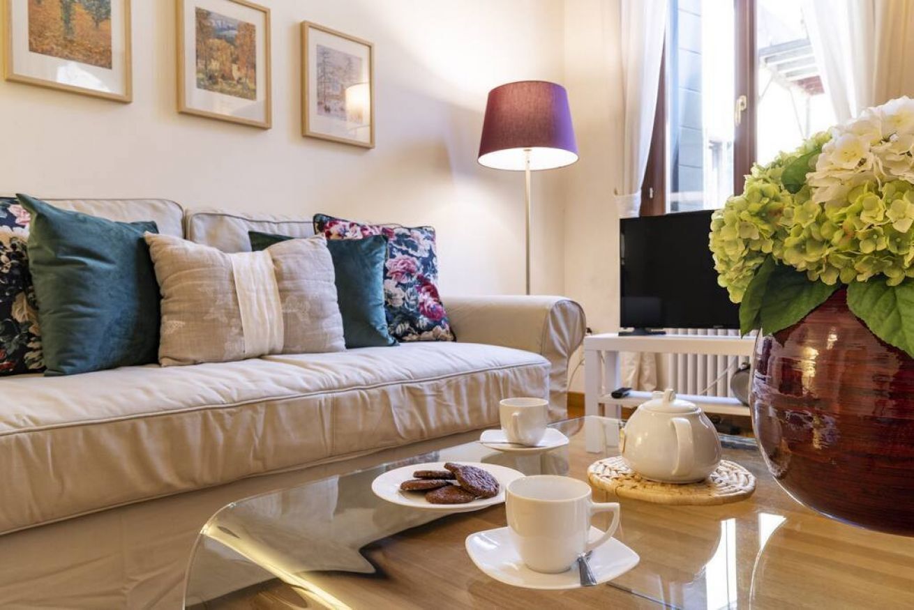 Un accogliente soggiorno con un divano, un tavolino da caffè con un vassoio di biscotti e tazze, una lampada e un vaso di fiori.