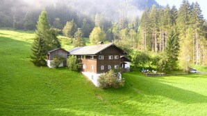 A wooden cabin with a sloped roof, surrounded by lush green fields and tall pine trees. - Mountain-view Cottage 15 Beds-pets Welcome (Bramberg am Wildkogel)