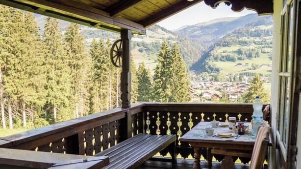 A wooden deck with a bench and table, overlooking a valley with houses and trees. - Mountain-view Cottage 15 Beds-pets Welcome (Bramberg am Wildkogel)