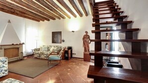 A living room with a wooden staircase, a sofa, a rug, and a statue.