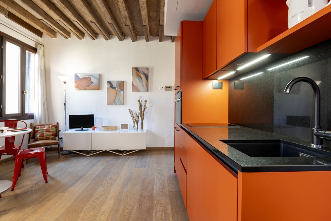 Una cucina moderna con mobili arancio, un piano di lavoro nero e un lavandino in acciaio inossidabile.
