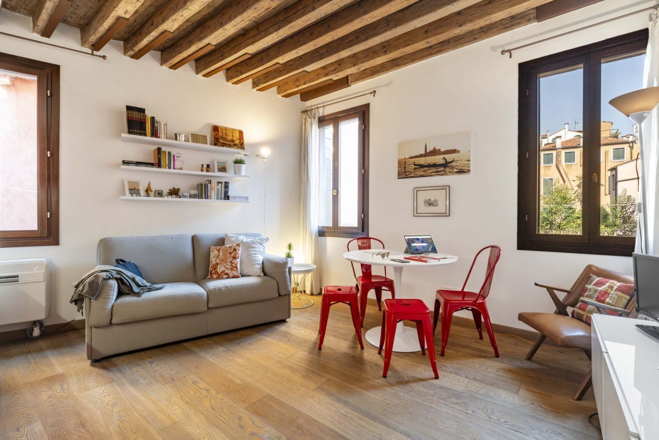Un soggiorno accogliente con soffitto in legno, un divano grigio, poltrone rosse e un tavolo bianco.