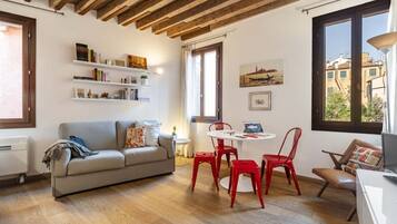 Un soggiorno accogliente con soffitto in legno, un divano grigio, poltrone rosse e un tavolo bianco.