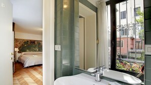 Ein Badezimmer mit einem weißen Waschbecken, einem Spiegel und einem Fenster mit Blick auf Gebäude.