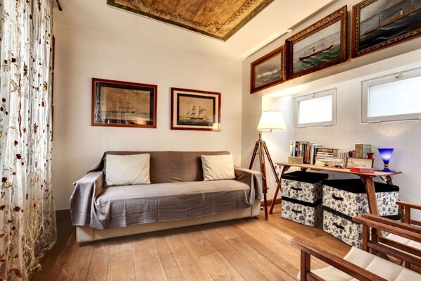 Una sala de estar acogedora con un sofá, piso de madera, cuadros enmarcados y una lámpara.