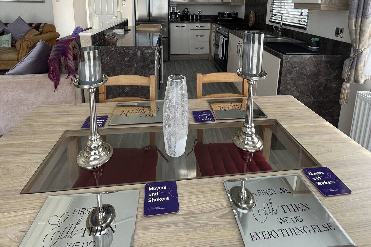 A modern kitchen with stainless steel appliances, a dining area with a glass table, and a living room with a sofa and decorative pillows.